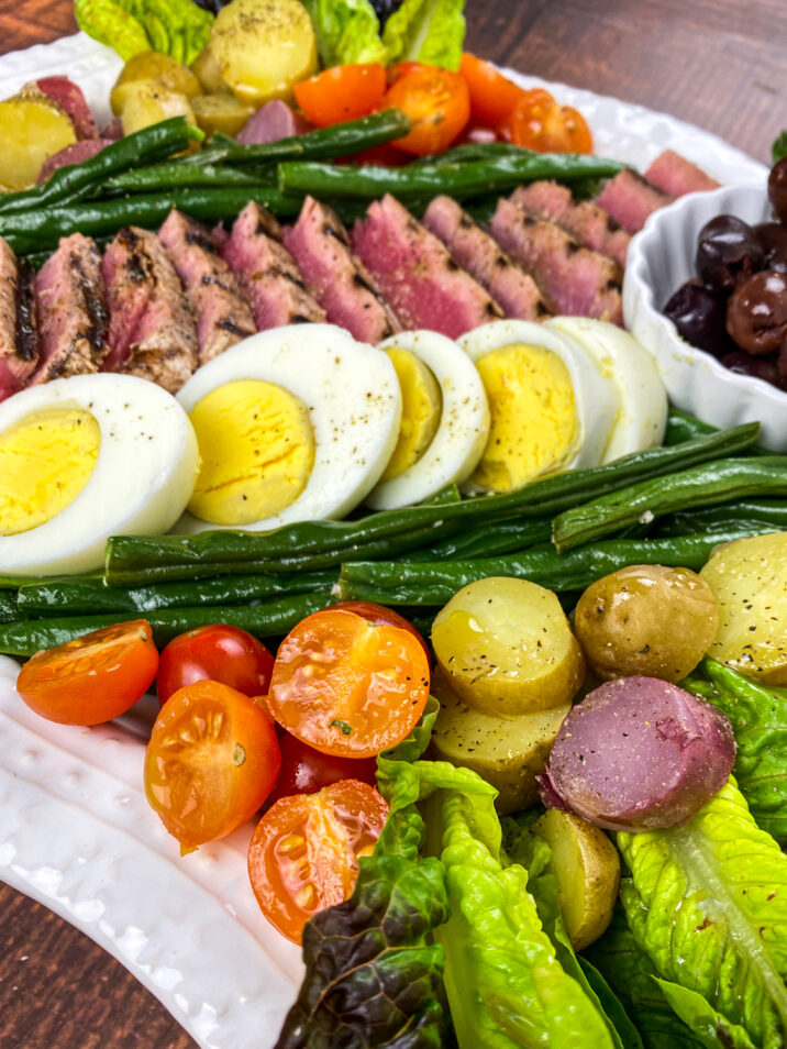 Niçoise Salad is a French composed salad, made of tomatoes, hard-boiled eggs, Niçoise olives and tuna. This version features seared Ahi Tuna.