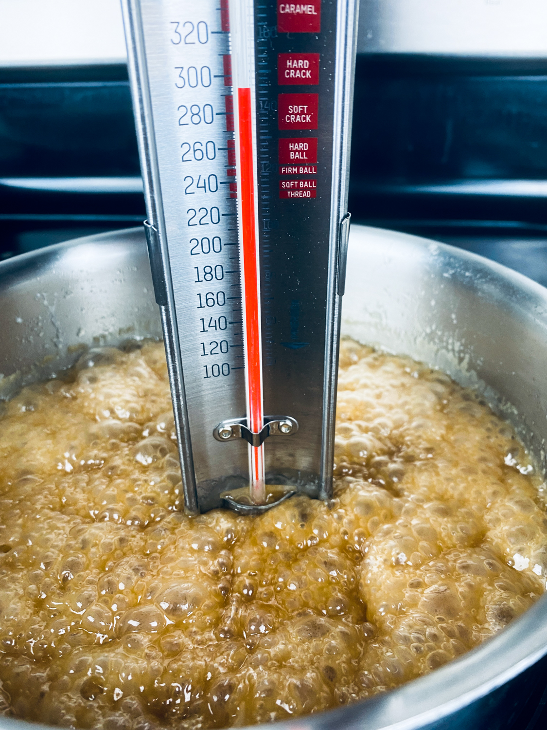 The candy mixture is boiling and temperature on the candy thermometer shows it has reached the hard crack stage.