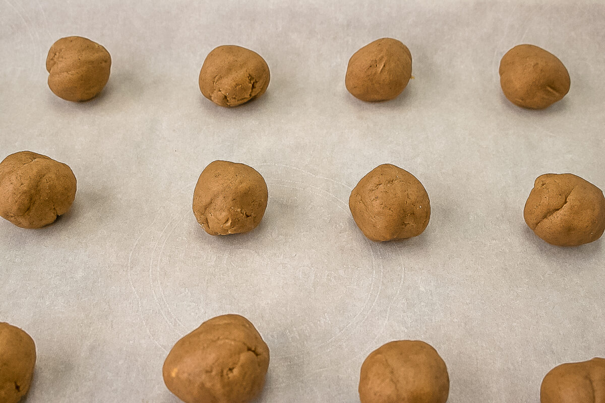 Spice dough being rolled into balls for baking and placed in a cookie sheet lined with parchment paper.