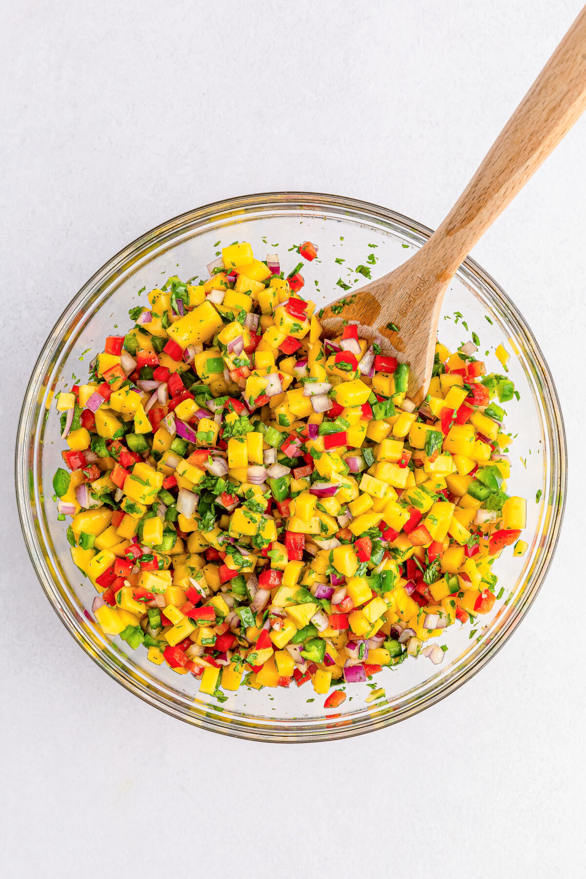 Mango salsa combined together in a large mixing bowl using a wooden spoon.